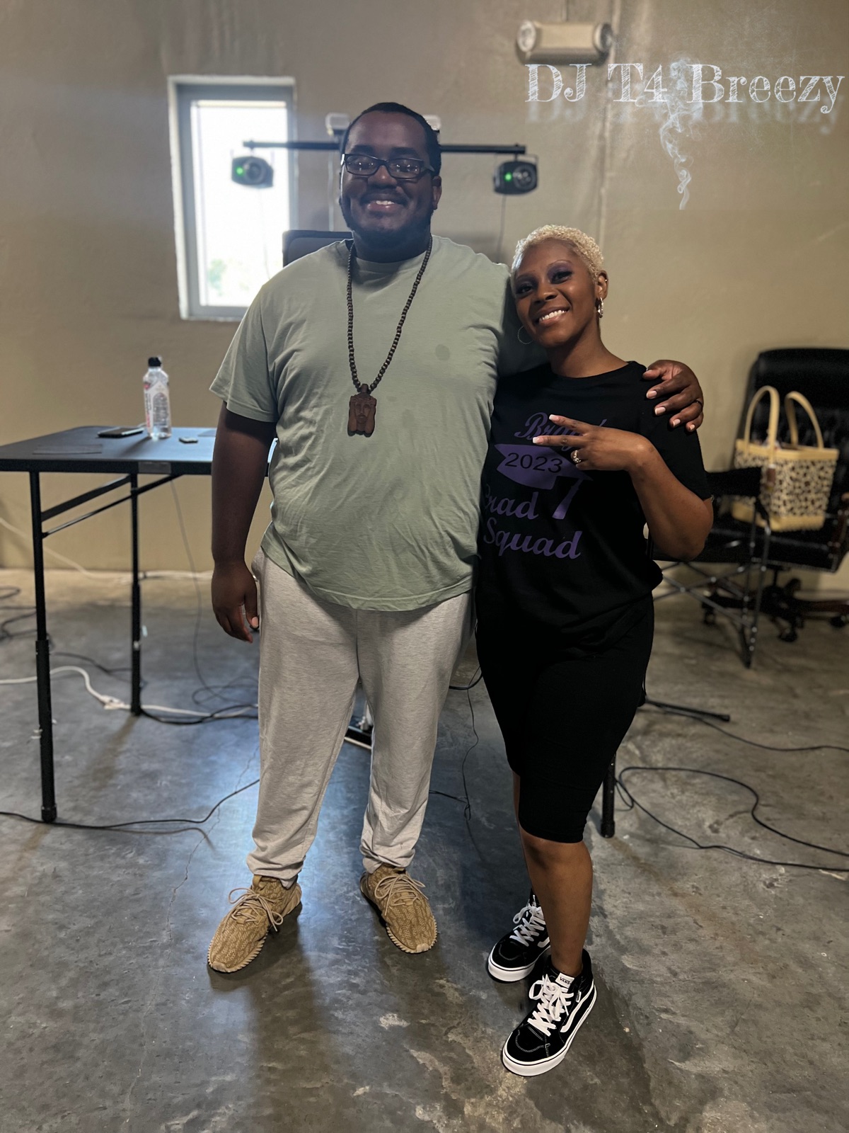 DJ T4 Breezy with a smiling guest in front of the DJ lights at an event